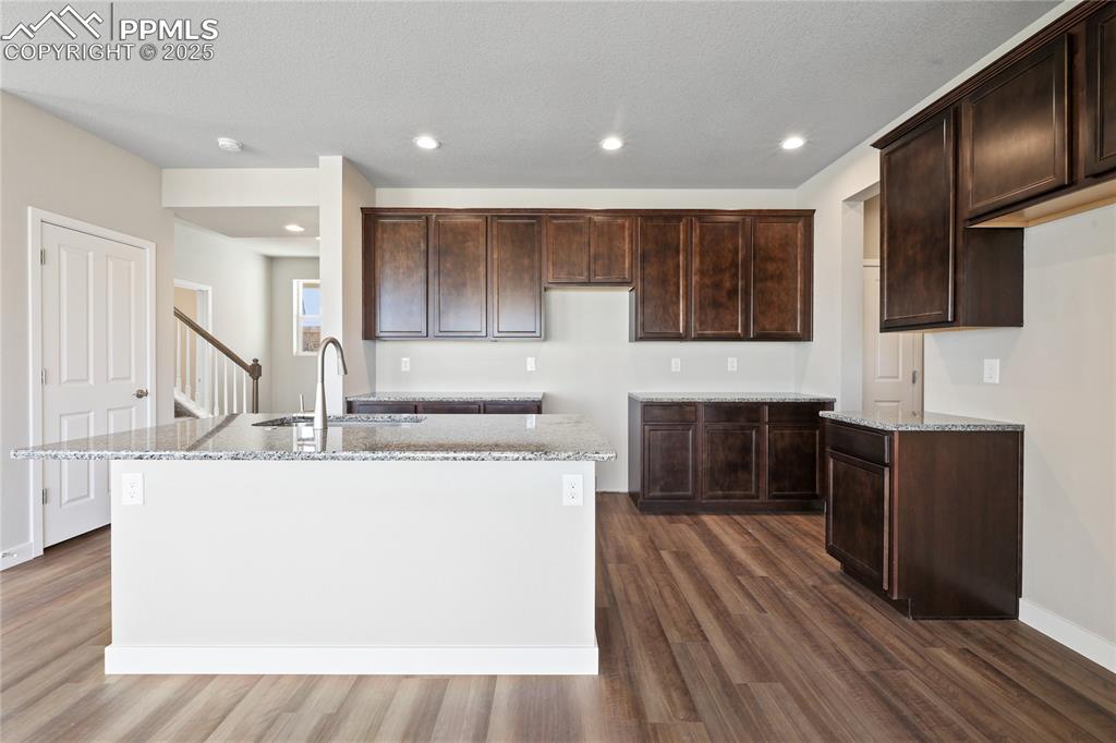 Image 12 of 25: Kitchen featuring recessed lighting, an island with sink, and dark brown ca