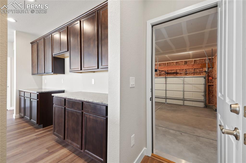 Image 15 of 25: Kitchen with dark brown cabinetry, light stone countertops, recessed lighti