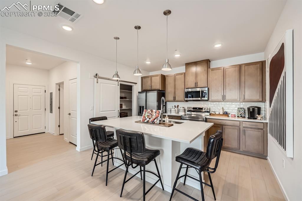 Image 3 of 9: Kitchen featuring stainless steel appliances, a barn door, backsplash, a br