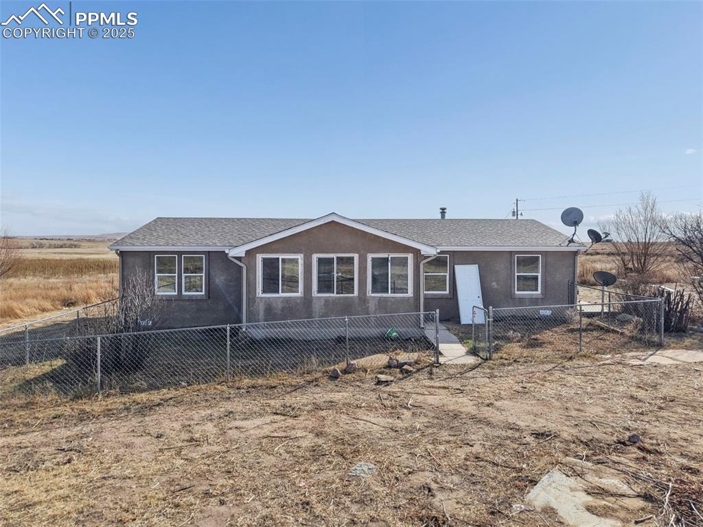 Caption: View of front of house featuring a fenced front yard, stucco siding, and a shingled roof