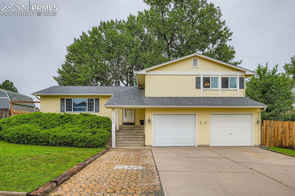 Caption: Tri-level home with a shingled roof, driveway, a garage, and stucco siding