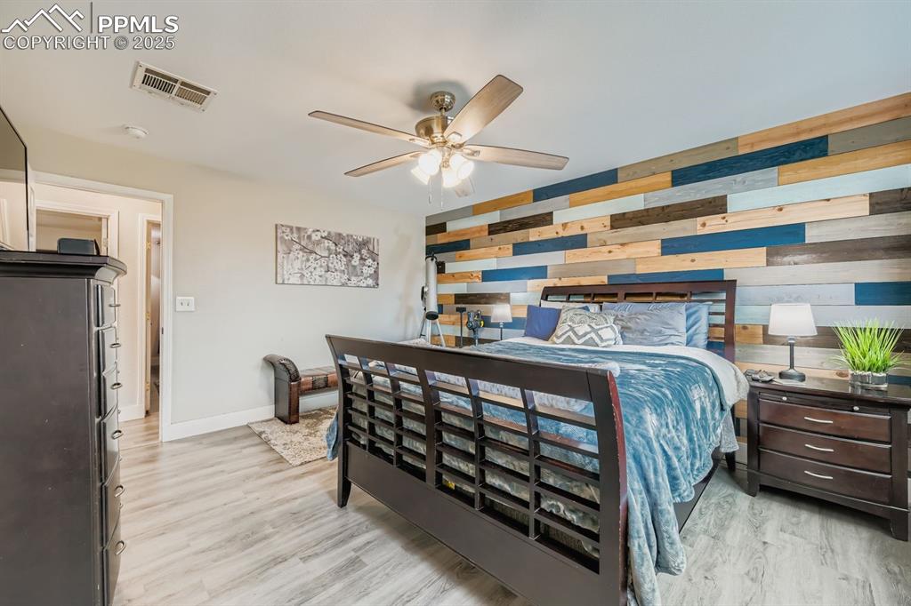 Image 13 of 27: Bedroom featuring wooden walls, light wood-type flooring, and ceiling fan