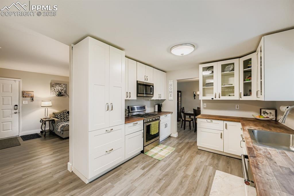 Image 8 of 27: Kitchen with glass insert cabinets, white cabinetry, appliances with stainl