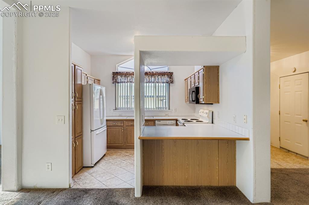 Image 11 of 29: Kitchen featuring brown cabinets, light tile patterned floors, a peninsula,