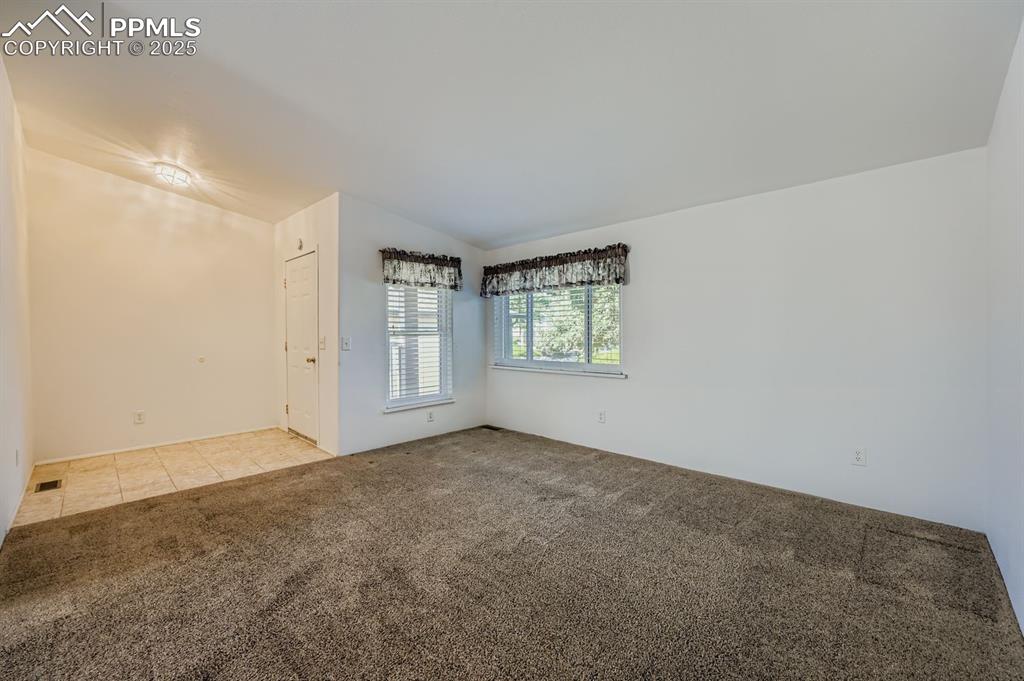 Image 8 of 29: Spare room featuring light colored carpet, lofted ceiling, and light tile p
