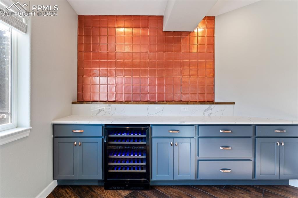 Image 40 of 50: Bar with beverage cooler, dark wood-style floors, a bar, decorative backspl
