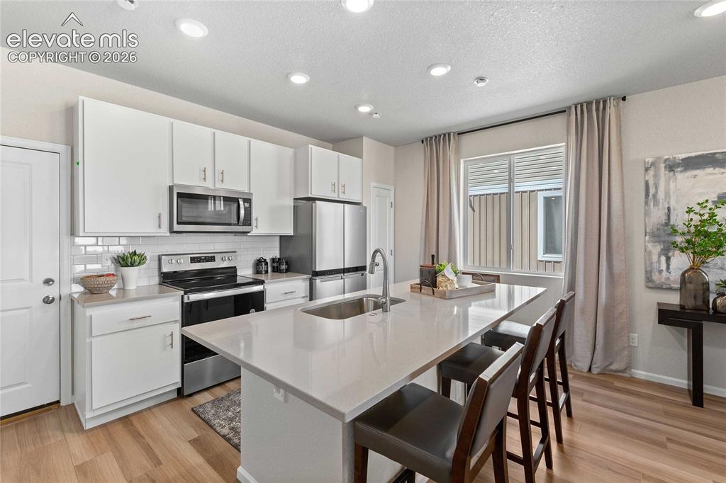 Image 10 of 25: Kitchen featuring stainless steel appliances, white cabinetry, a subway til