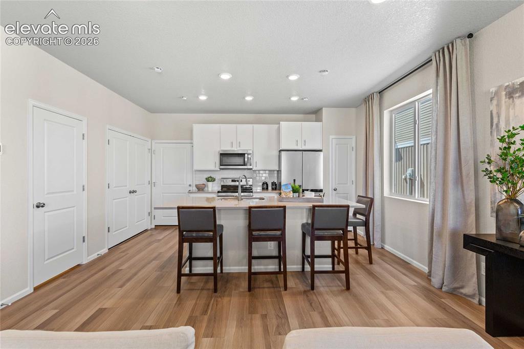 Image 6 of 25: Open-concept living space with wood-finish flooring, recessed lighting, whi