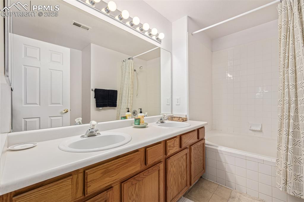 Image 13 of 24: Full bathroom with tiled shower / bath combo, double vanity, and light tile