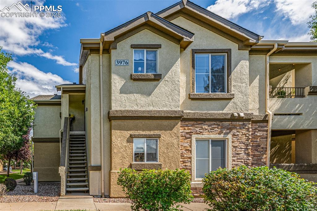 Image 2 of 24: View of front of property with stucco siding, stone siding, stairway, and a