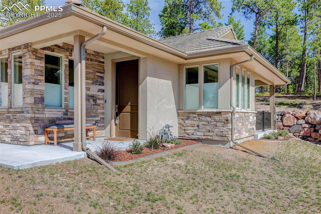 Image 24 of 32: Entrance to property featuring stone siding, stucco siding, a yard, and cov