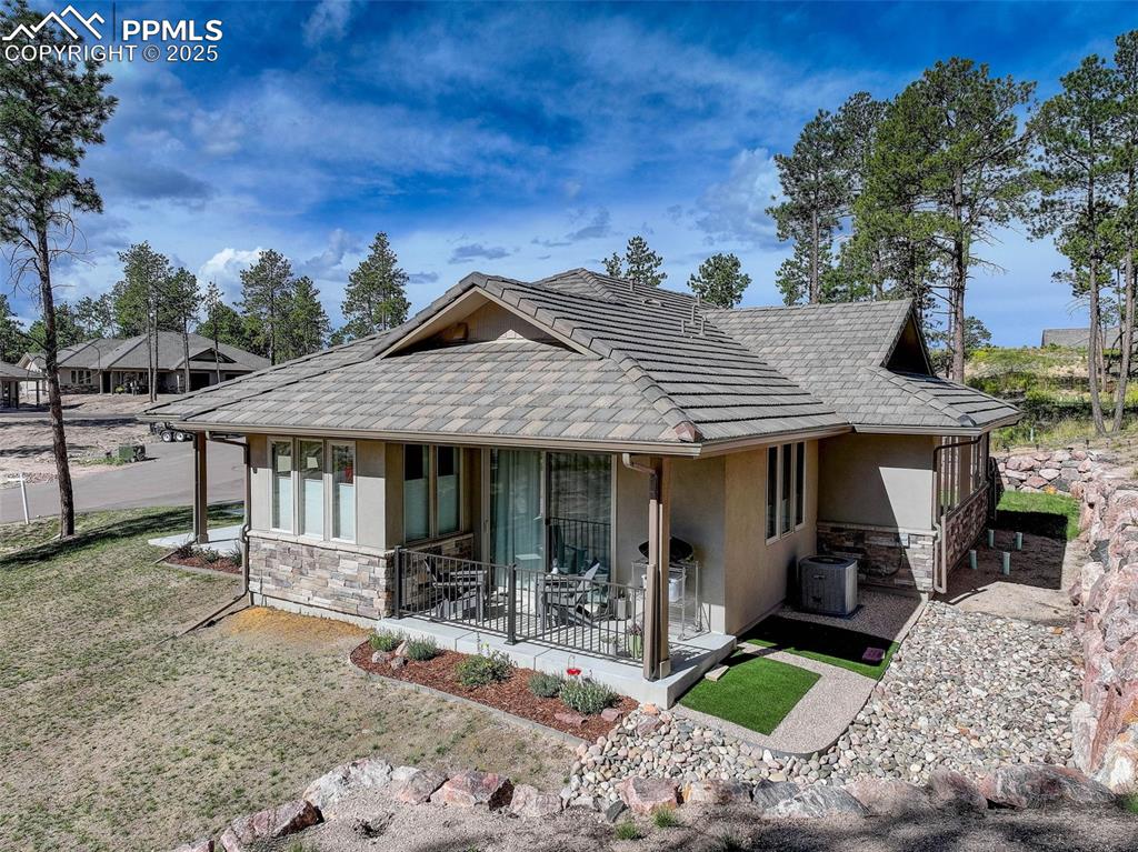 Image 27 of 32: Back of property with stone siding, stucco siding, and a lawn