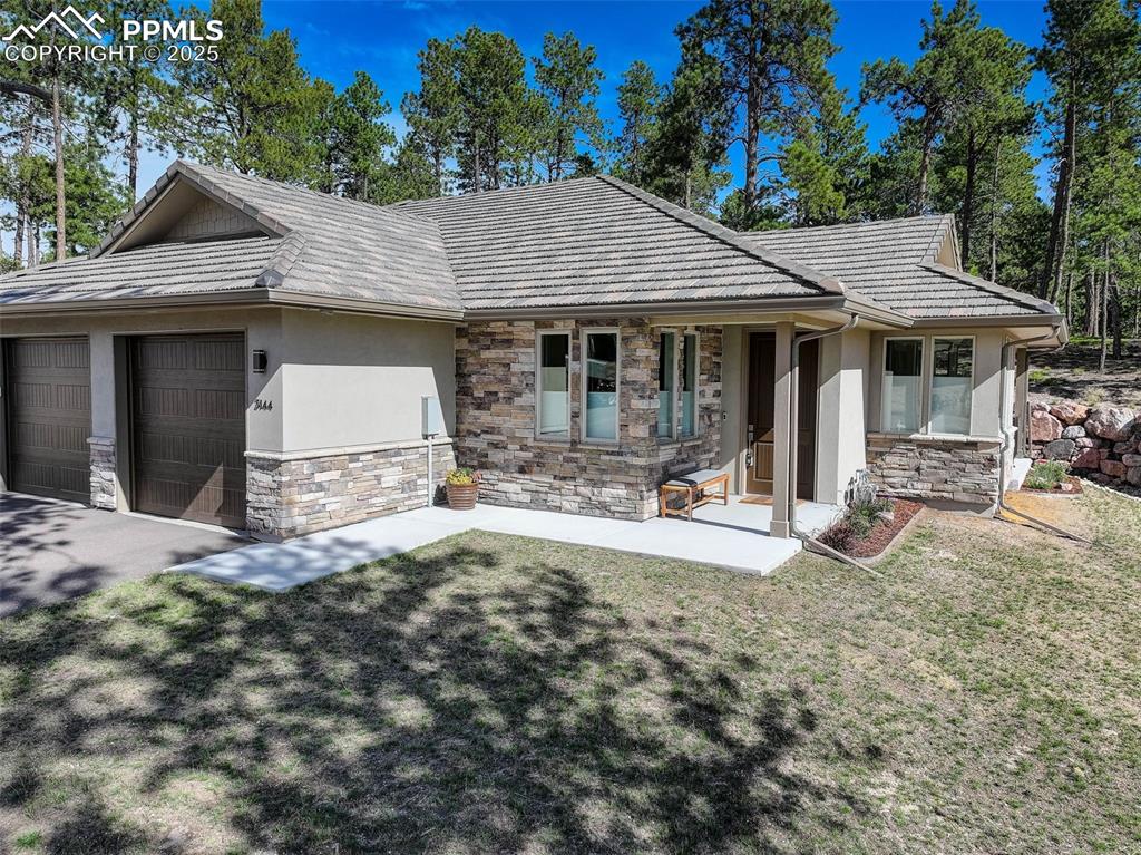 Image 3 of 32: View of front of home featuring a garage, stucco siding, a front lawn, ston