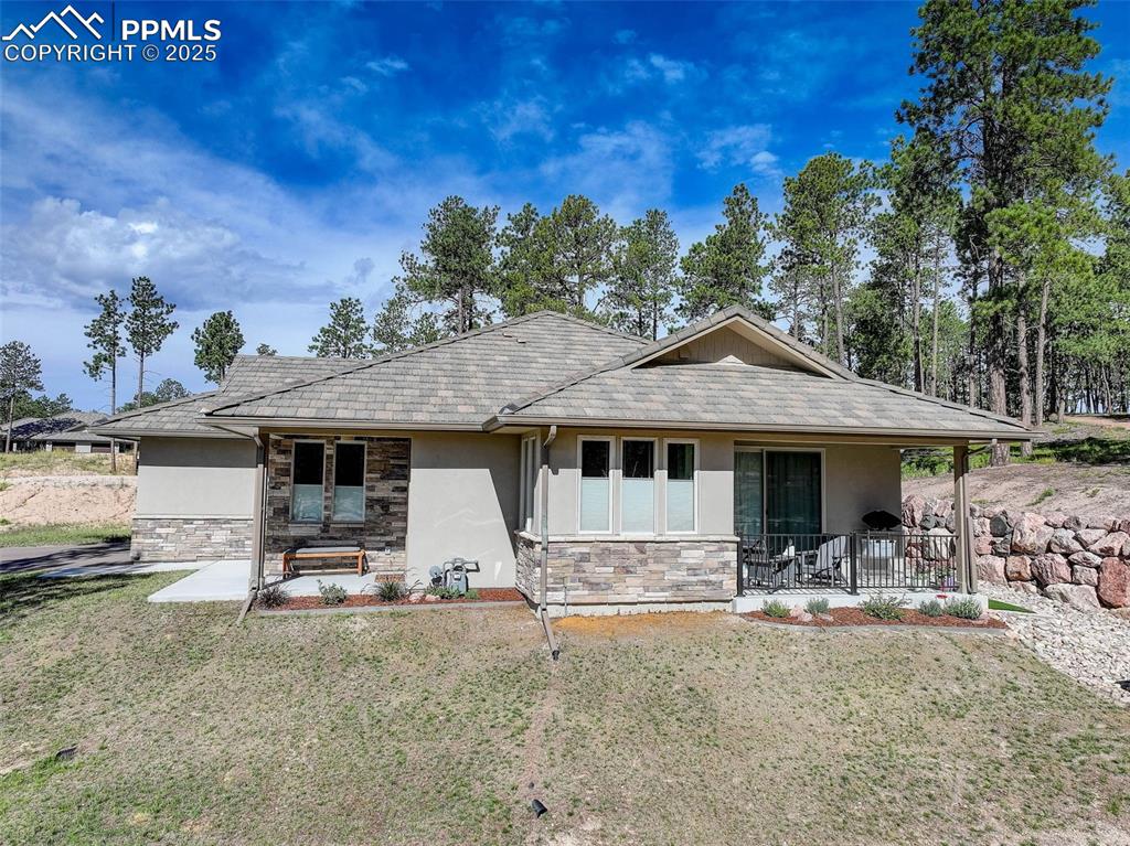 Image 4 of 32: Back of house featuring stucco siding, a lawn, and stone siding