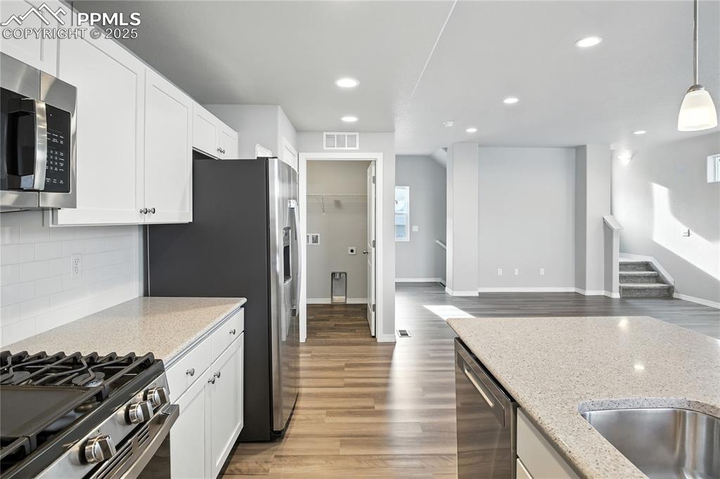 Image 8 of 28: Kitchen with white cabinets, light wood-style floors, light stone counterto