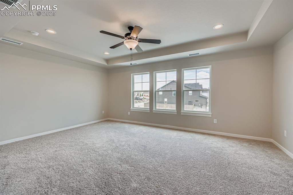 Image 14 of 28: Empty room featuring a tray ceiling, light colored carpet, ceiling fan, and
