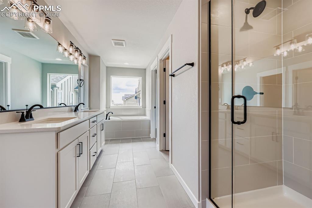 Image 18 of 28: Full bath featuring a stall shower, double vanity, a garden tub, and tile p