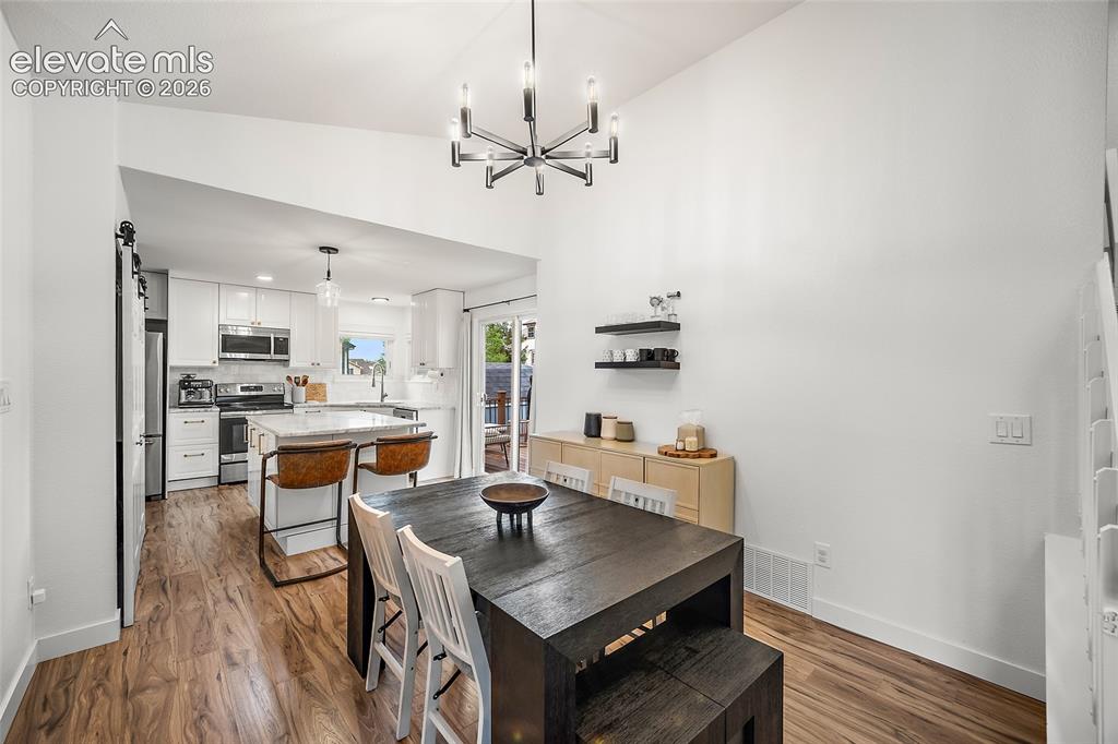 Image 14 of 50: Dining area featuring a vaulted ceiling with a contemporary chandelier, woo