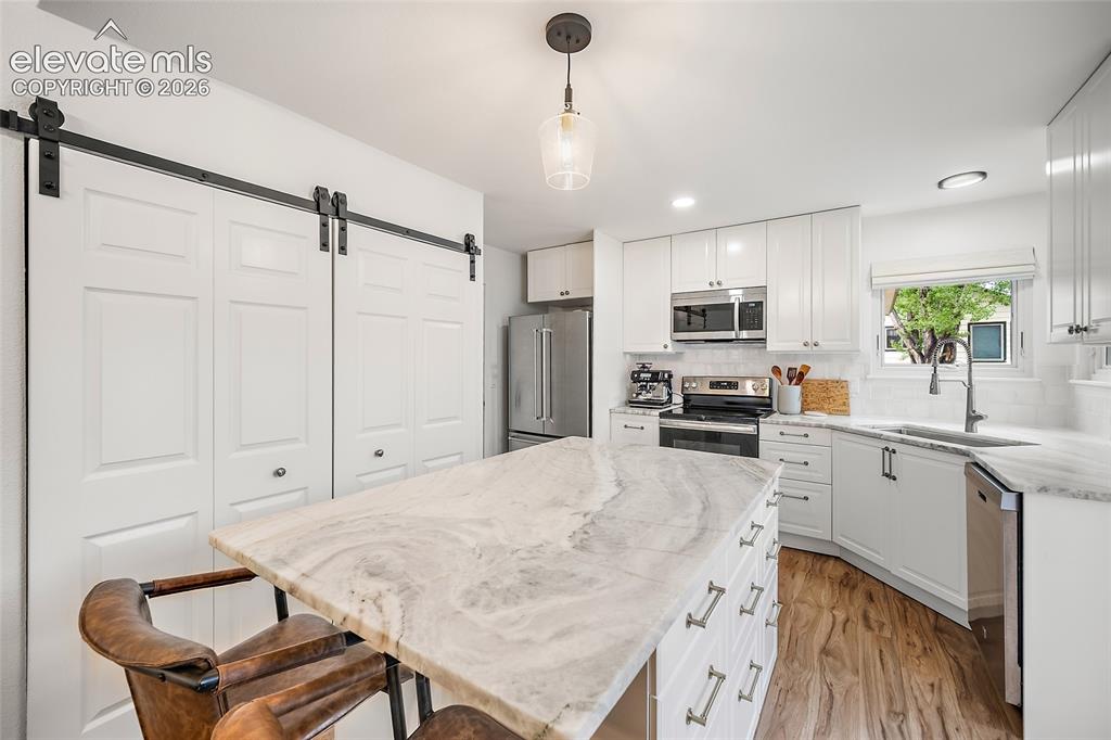 Image 15 of 50: Kitchen featuring a stone-finish island with seating, white shaker-style ca