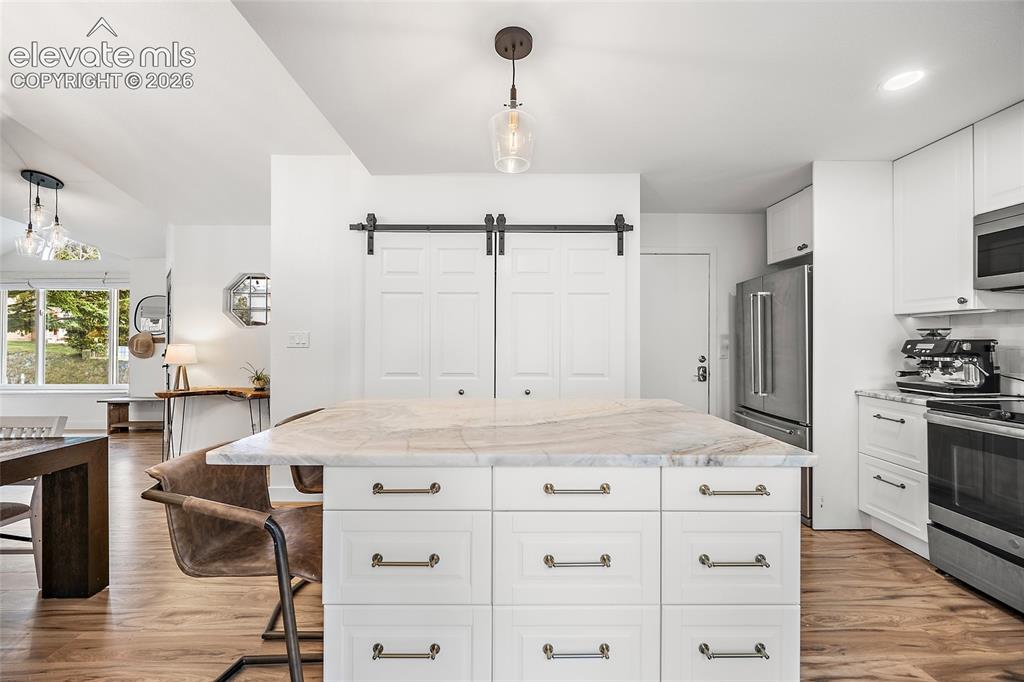 Image 16 of 50: Kitchen island with a light-toned stone countertop, white shaker-style cabi