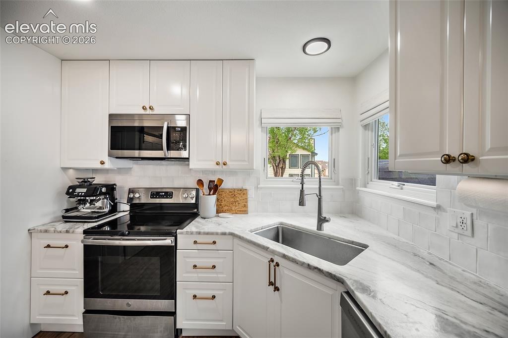 Image 17 of 50: Modern kitchen featuring warm white shaker cabinetry with brass hardware, s