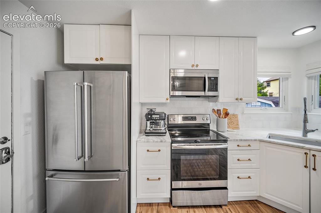 Image 19 of 50: Kitchen featuring white shaker cabinetry with brass hardware, stainless ste