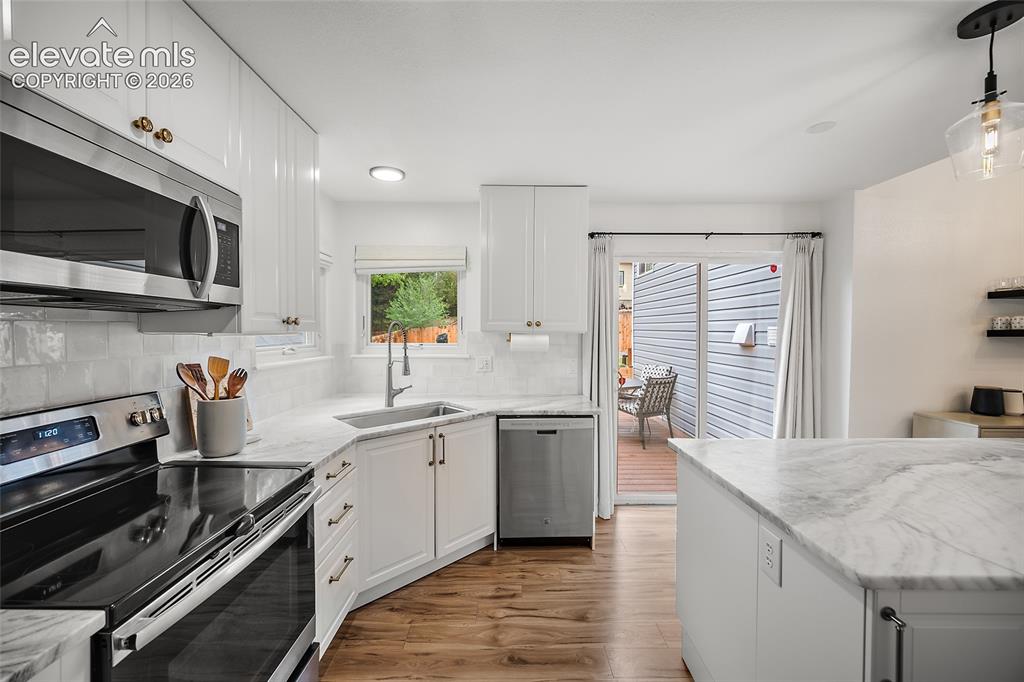 Image 20 of 50: Bright kitchen featuring white cabinetry, stainless steel appliances, marbl