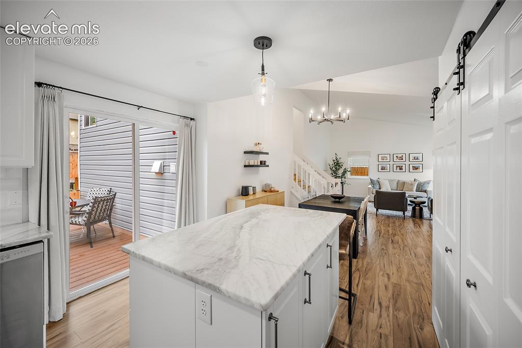 Image 21 of 50: Kitchen island with a marbled countertop, white cabinetry, and pendant ligh