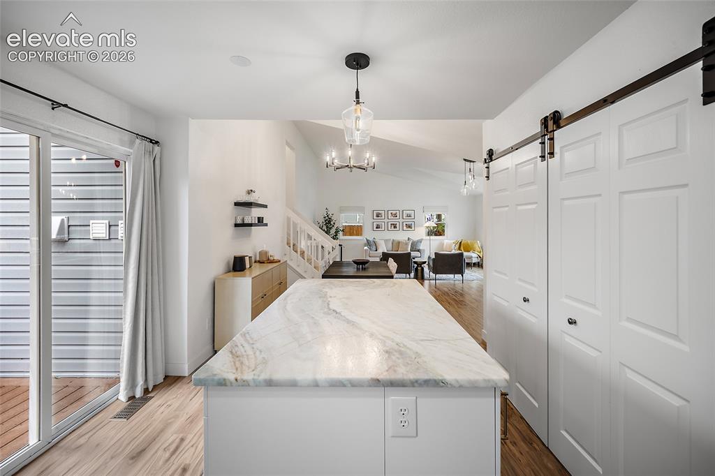 Image 22 of 50: Kitchen island with a light-toned stone countertop, white cabinetry, and wo