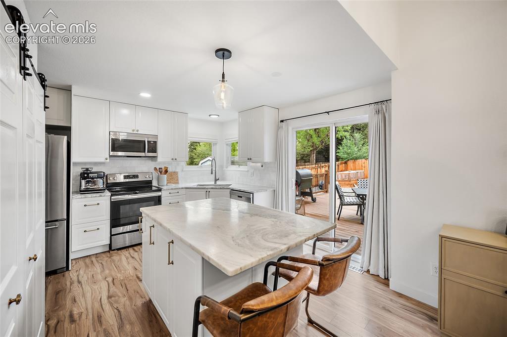 Image 23 of 50: Modern kitchen featuring white cabinetry, stainless steel appliances, a cen