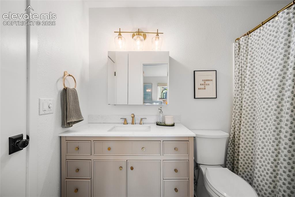 Image 28 of 50: Bathroom featuring a light-toned vanity with gold-finish hardware, a white 