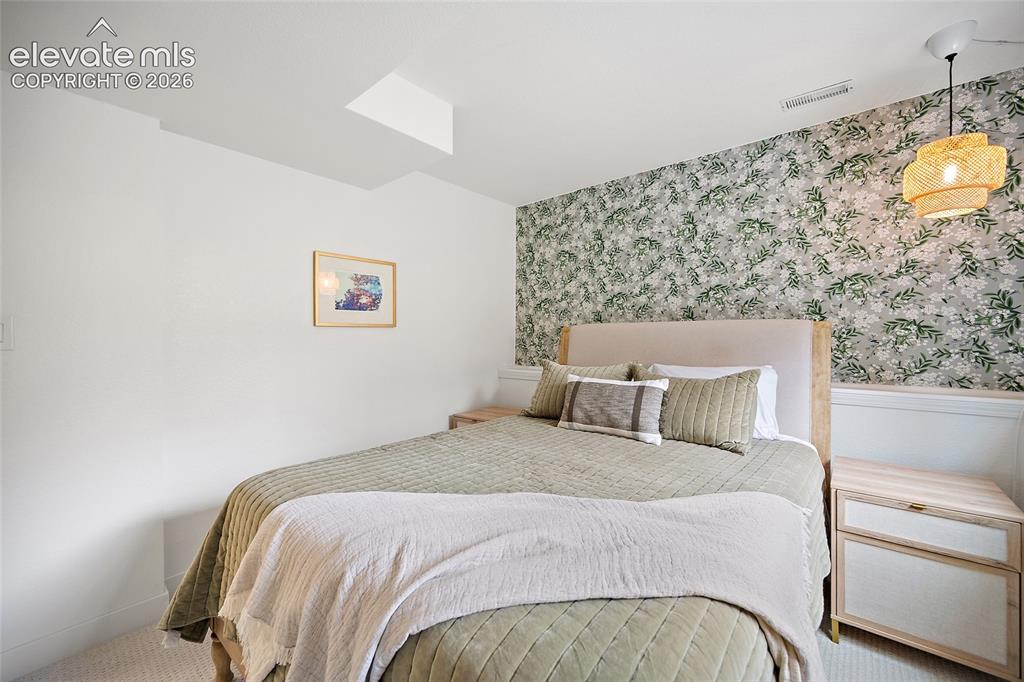 Image 37 of 50: Bedroom featuring an accent wall with botanical-patterned wallpaper, wainsc
