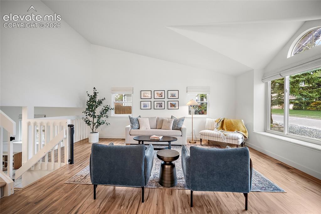 Image 6 of 50: Spacious living area featuring vaulted ceilings, wood-finish flooring, and 