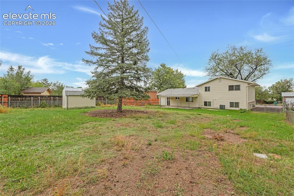 Image 26 of 29: Expansive grassy yard with mature trees, detached storage shed, and fenced 