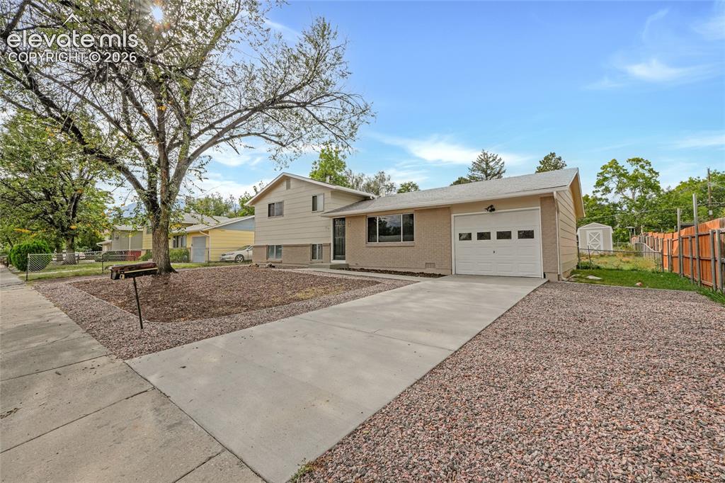 Image 3 of 29: Front exterior with an attached garage, a concrete driveway, and a gravel f
