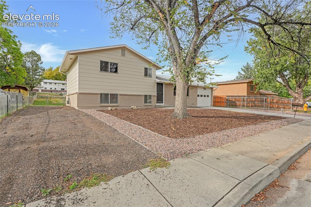Image 4 of 29: Split-level exterior with a one-car garage, front yard landscaping with roc