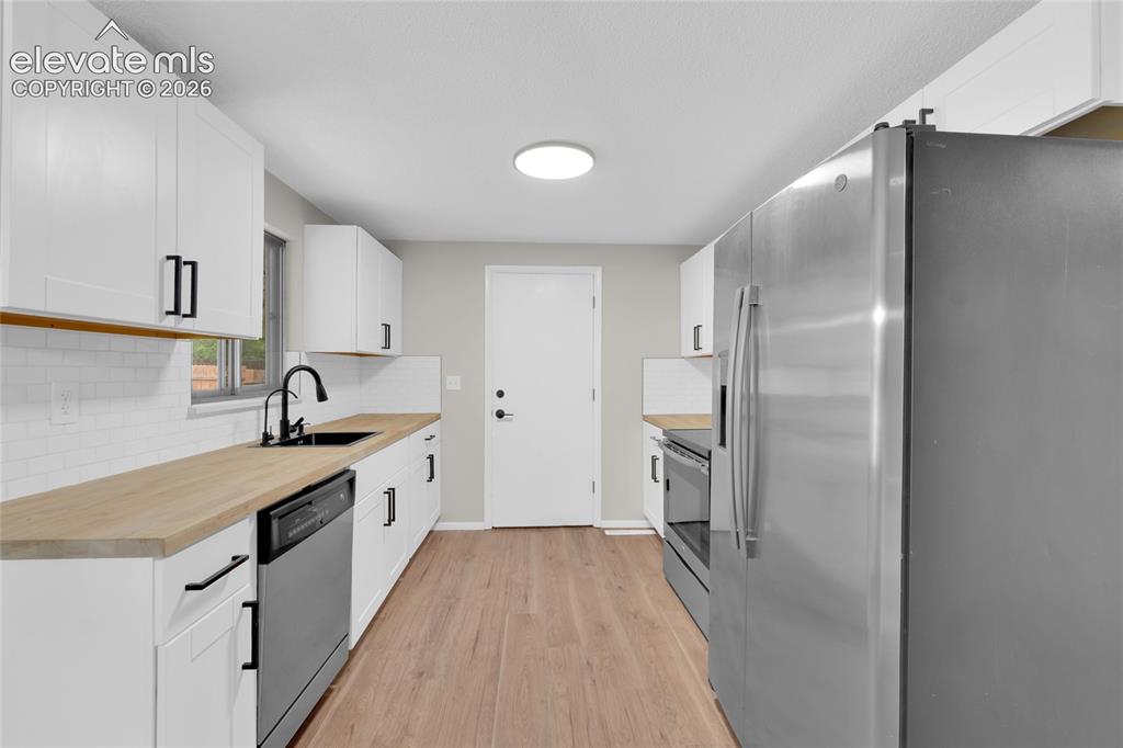Image 8 of 29: Kitchen featuring wood-finish flooring, white cabinetry with matte black ha