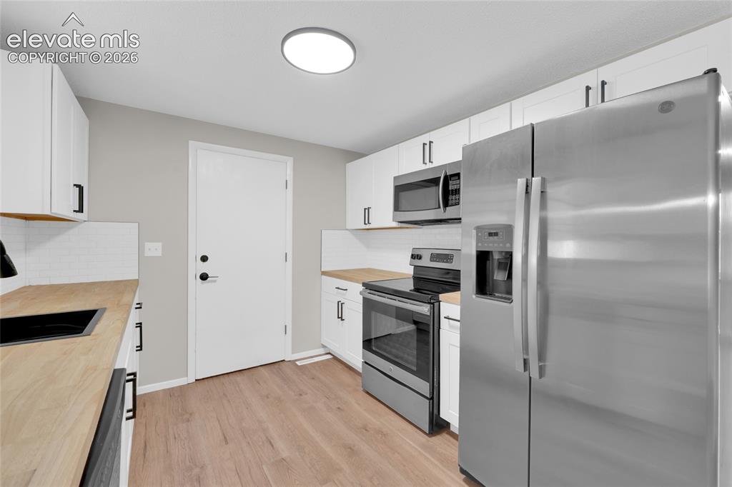 Image 9 of 29: Kitchen featuring wood-finish flooring, white cabinetry with black hardware