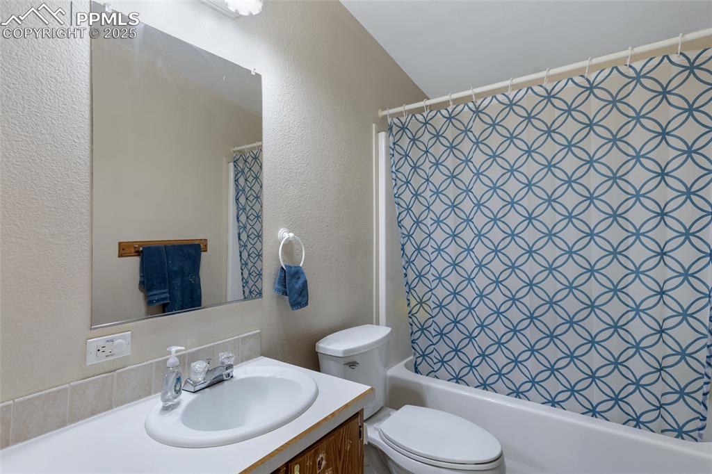 Image 13 of 24: Full bath featuring toilet, vanity, a textured wall, and shower / bathtub c