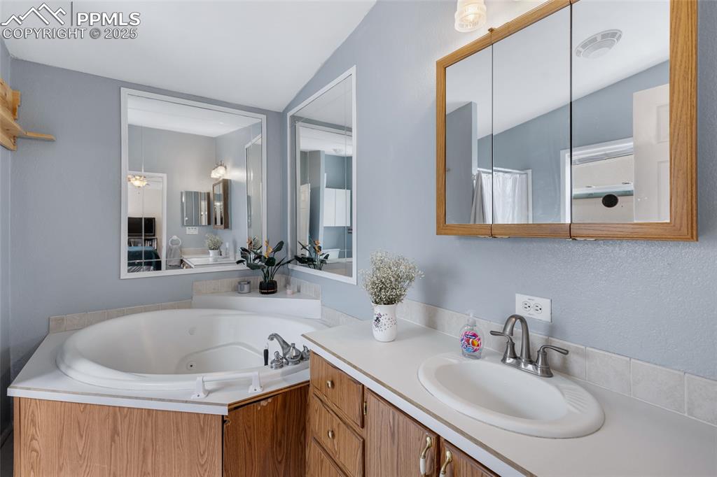 Image 18 of 24: Full bathroom featuring a tub with jets, vaulted ceiling, and vanity