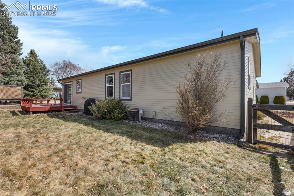 Image 22 of 24: Back of house featuring fence, a wooden deck, central AC unit, and a yard
