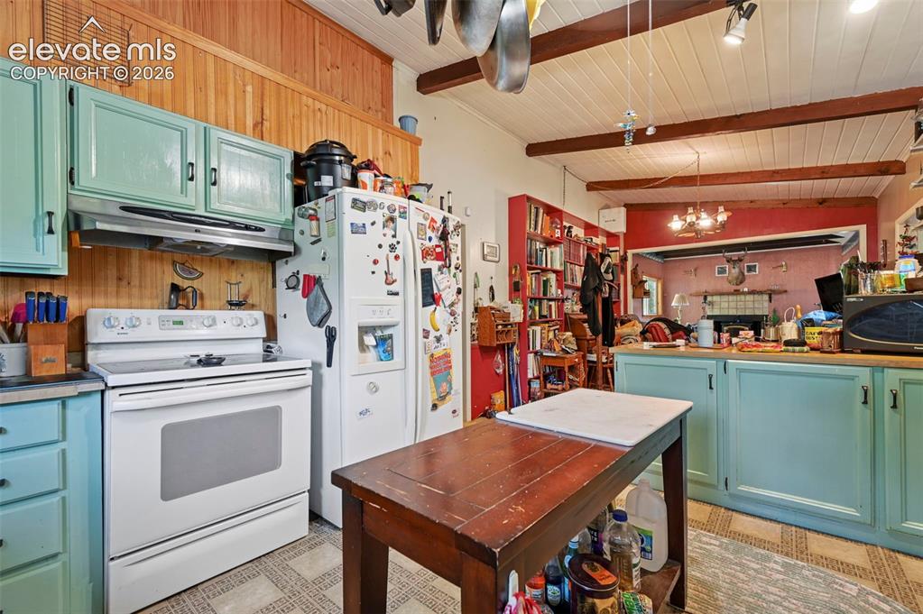 Image 5 of 29: Kitchen featuring wood-paneled walls, exposed ceiling beams, and a built-in