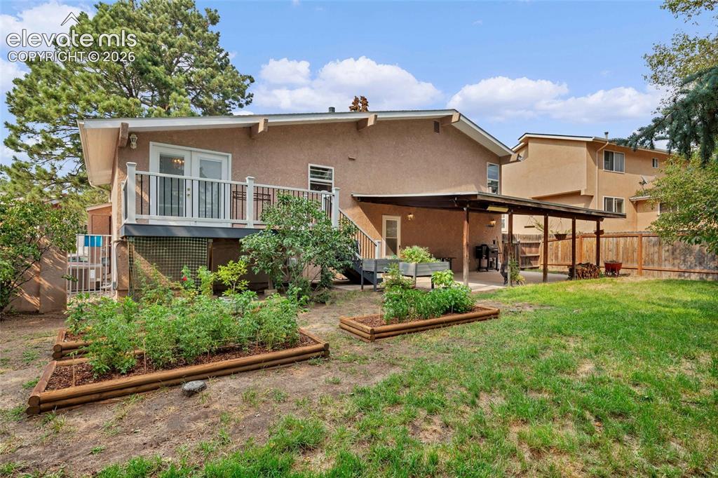 Image 35 of 44: Expansive backyard with a manicured lawn, tiered garden beds, and mature tr