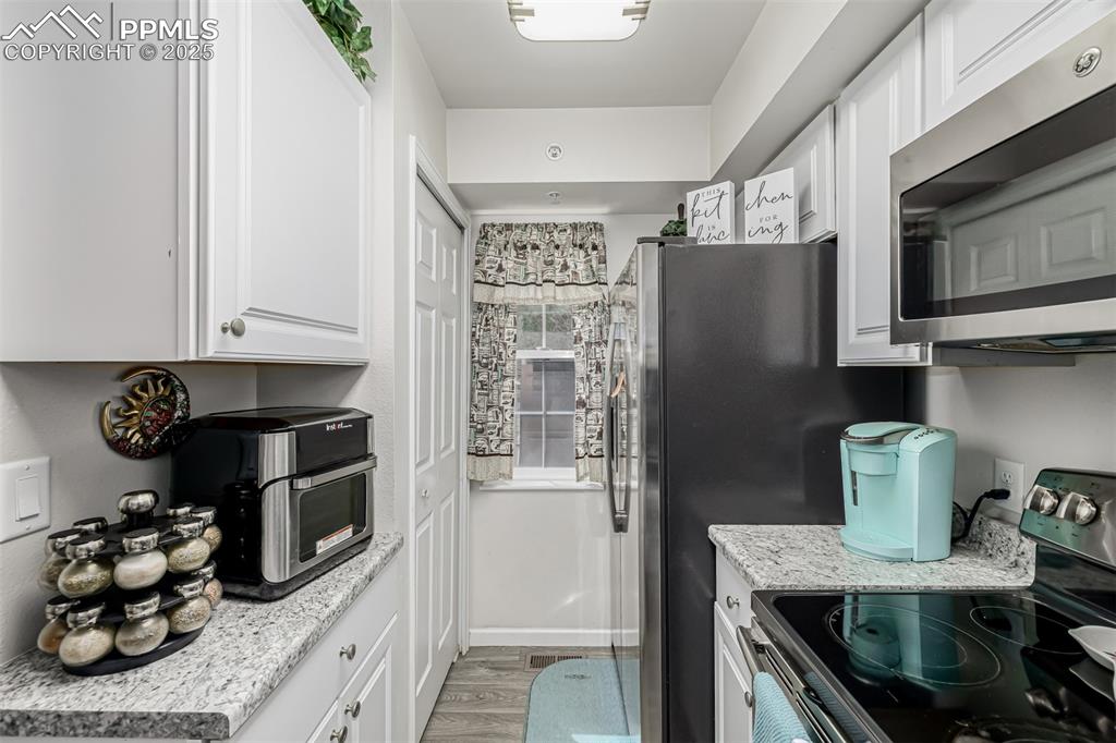 Image 11 of 47: Kitchen featuring stainless steel appliances, white cabinetry, light wood-t