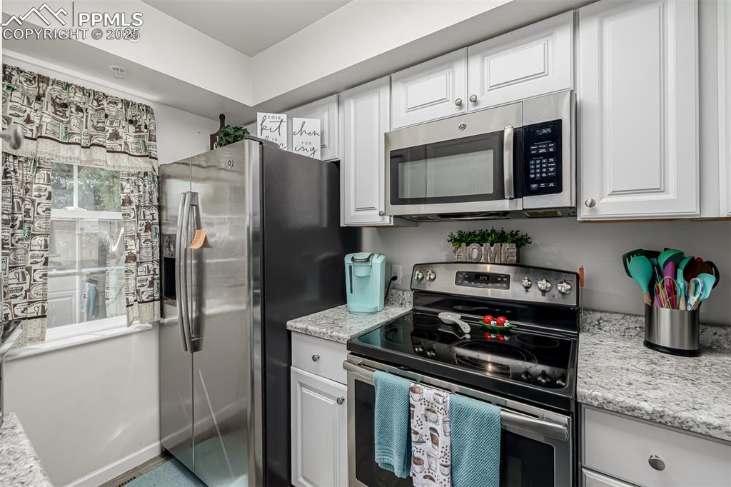 Image 12 of 47: Kitchen with stainless steel appliances, white cabinetry, and light stone c