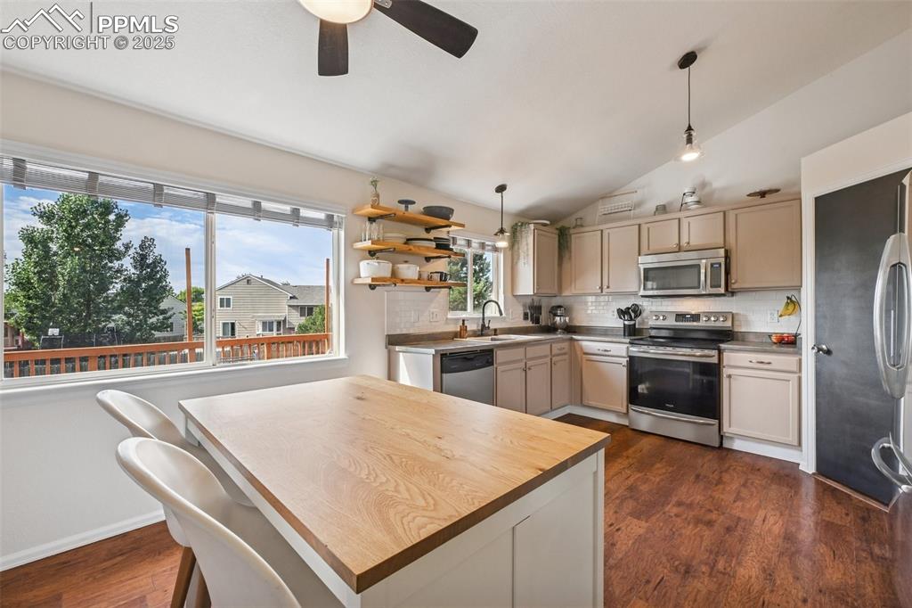 Image 8 of 38: Kitchen featuring stainless steel appliances, lofted ceiling, dark wood fin
