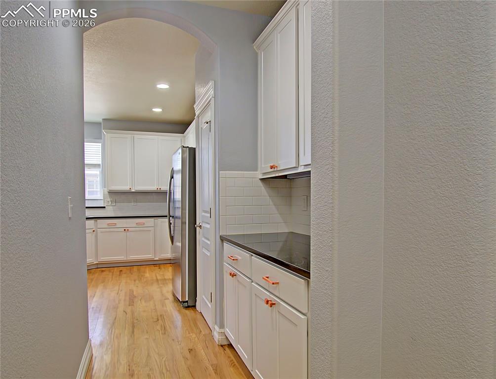 Image 14 of 27: Kitchen featuring a textured wall, dark countertops, white cabinets, light 