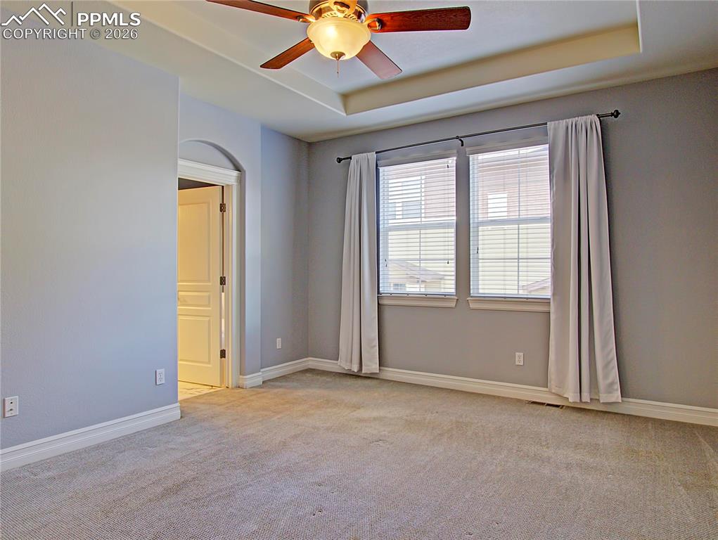 Image 16 of 27: Spare room featuring a raised ceiling, a ceiling fan, and light colored car