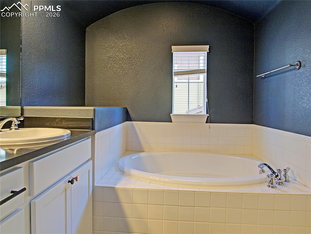 Image 17 of 27: Bathroom featuring a textured wall, a garden tub, vanity, and lofted ceilin