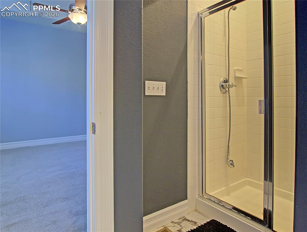 Image 18 of 27: Full bath with a textured wall, a shower stall, and a ceiling fan